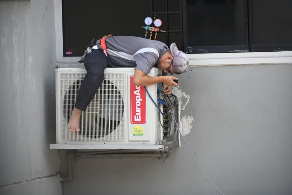 A technician skillfully repairing an outdoor air conditioning unit mounted on a building wall.